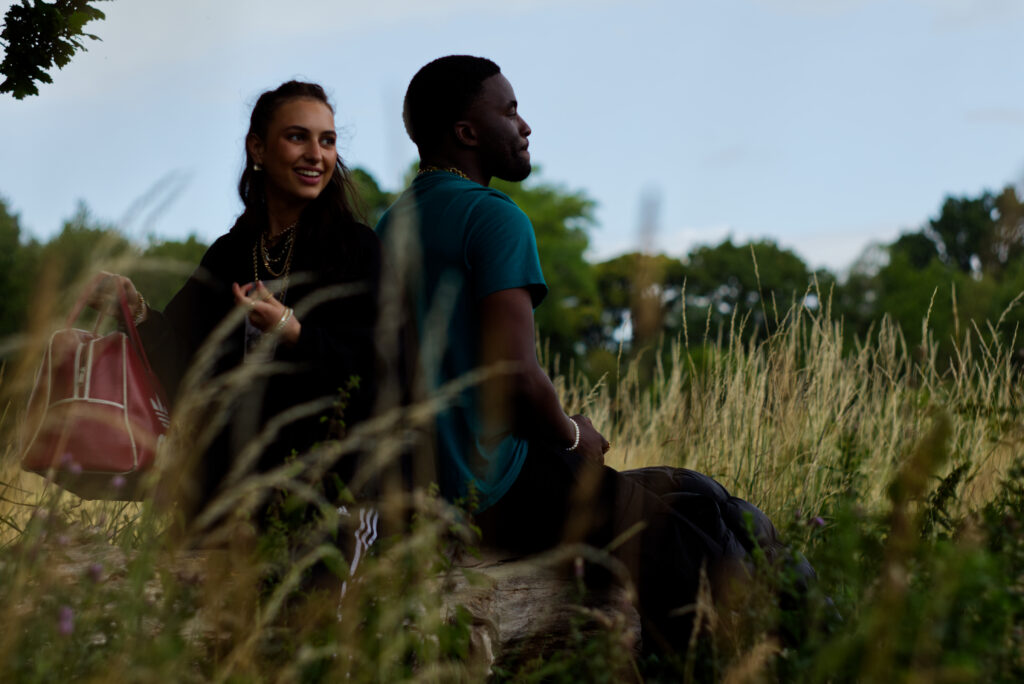 A screenshot from the film of actors Evans and Natalie sitting in long grass. 